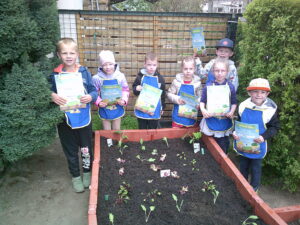 Foto von mehreren Kindern mit Urkunden, wie sie um ein Beet stehen.