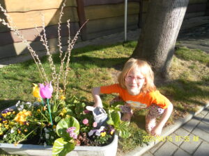 Foto von Kind mit Plüschhasen an einem Blumenbeet.